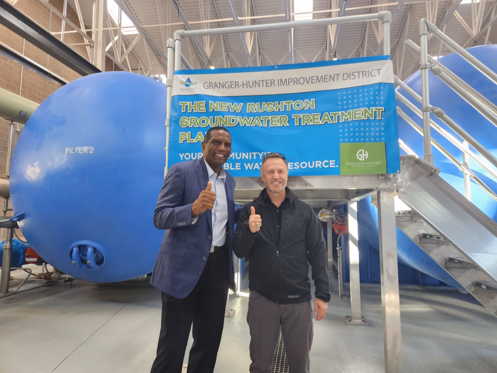 Two men pose in front of a sign announcing the opening of a new facility.